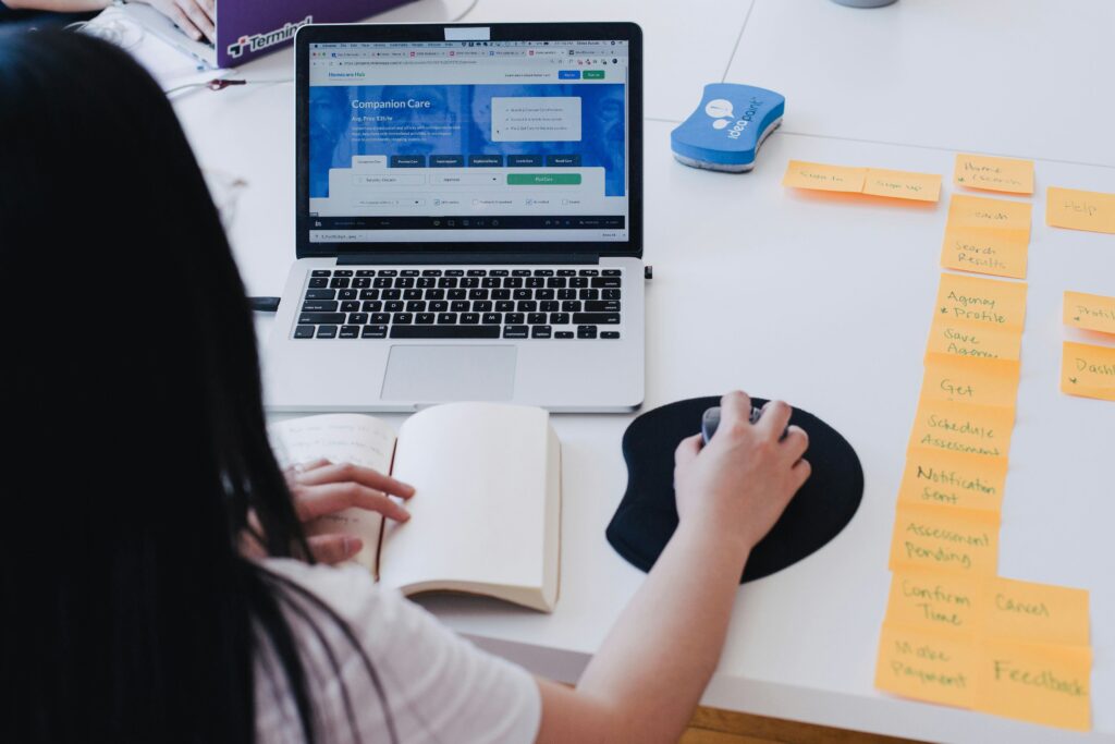 features a person at a laptop computer with sticky notes, notebook and a mouse.