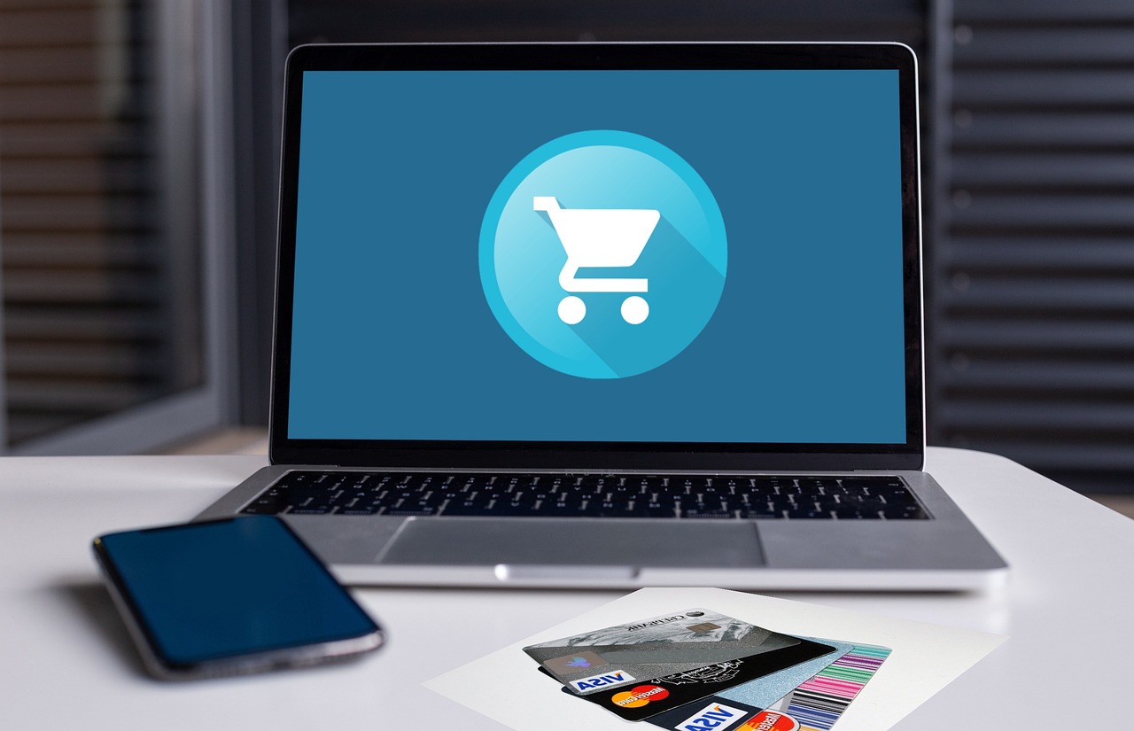 Image of a laptop with a blue shopping cart on the screen, in front of the laptop is a small stack of various debit cards.